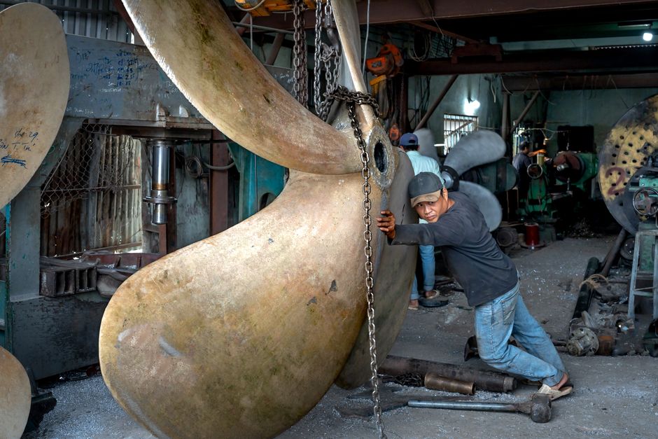 Worker adjusts massive ship propeller in industrial workshop, showcasing detailed craftsmanship.
