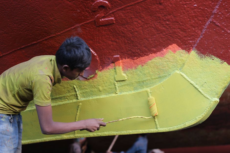 Man applying colorful paint to ship hull, blending red and green hues with precision.